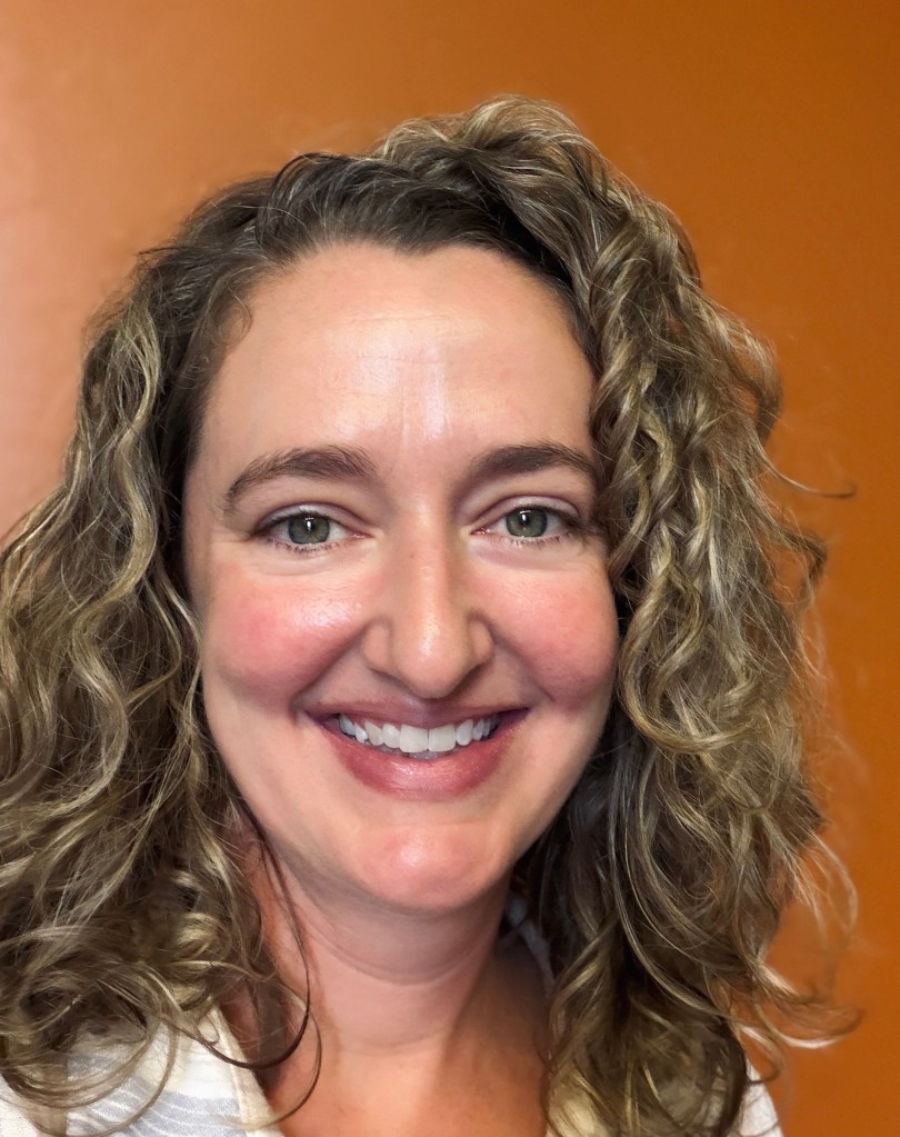 A woman with curly hair smiles warmly, against an orange background. The tone is friendly and approachable.